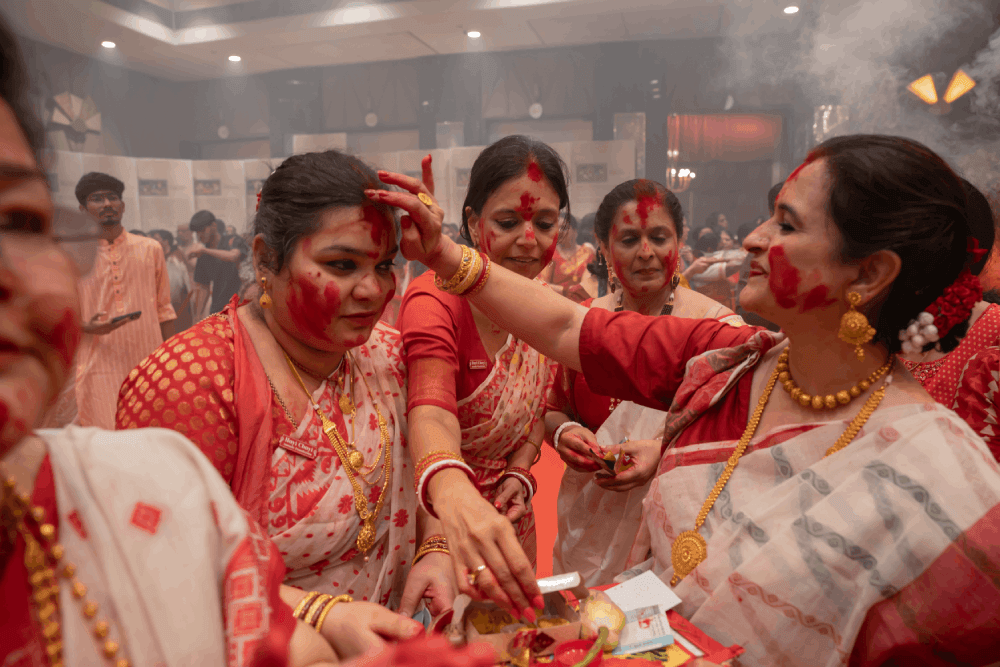 Women celebrating Sindoor Khela with vibrant red sindoor powder against bright natural lighting